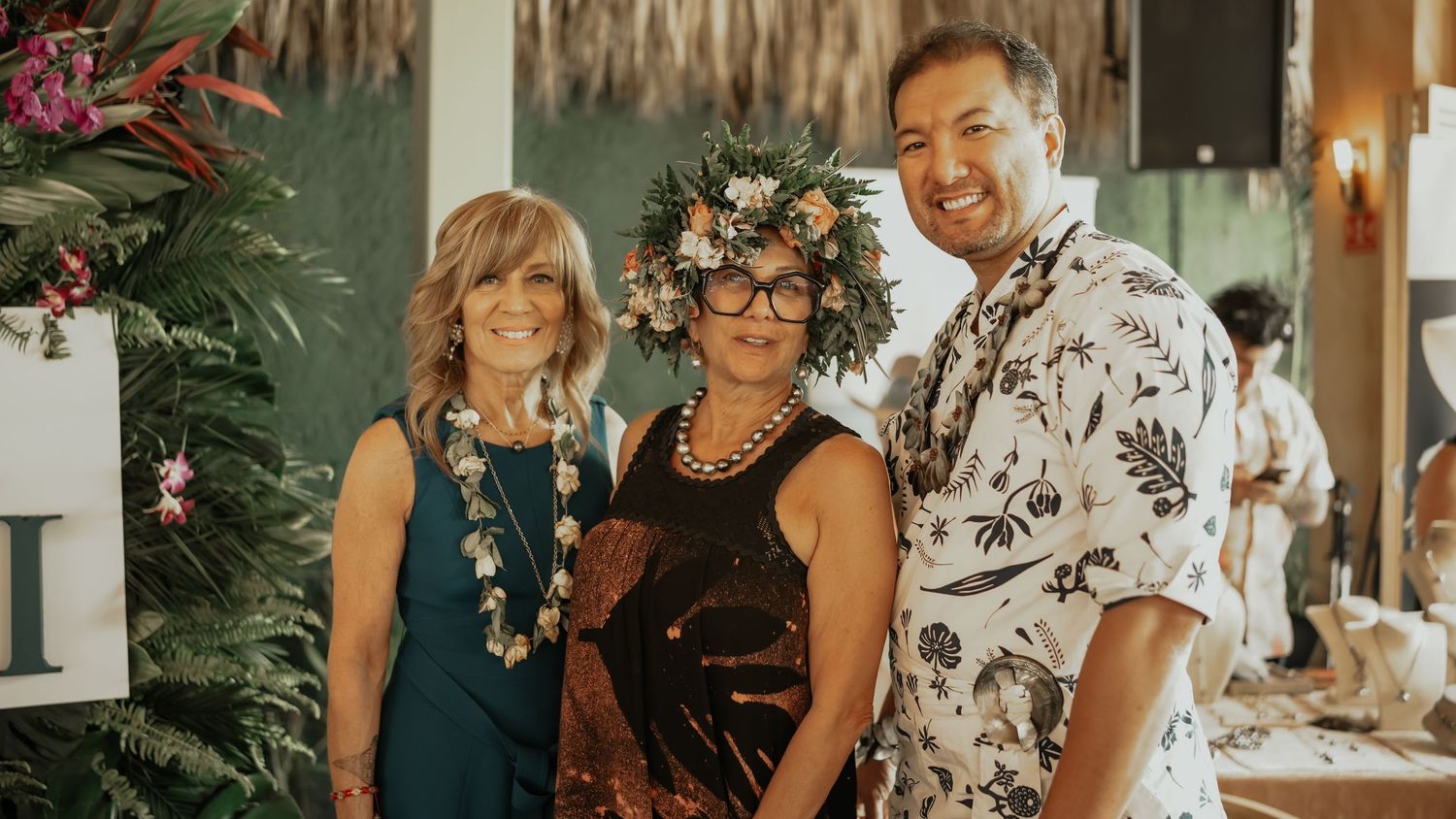 Three people posing together at a Tahiti tourism event, one wearing a floral headdress.