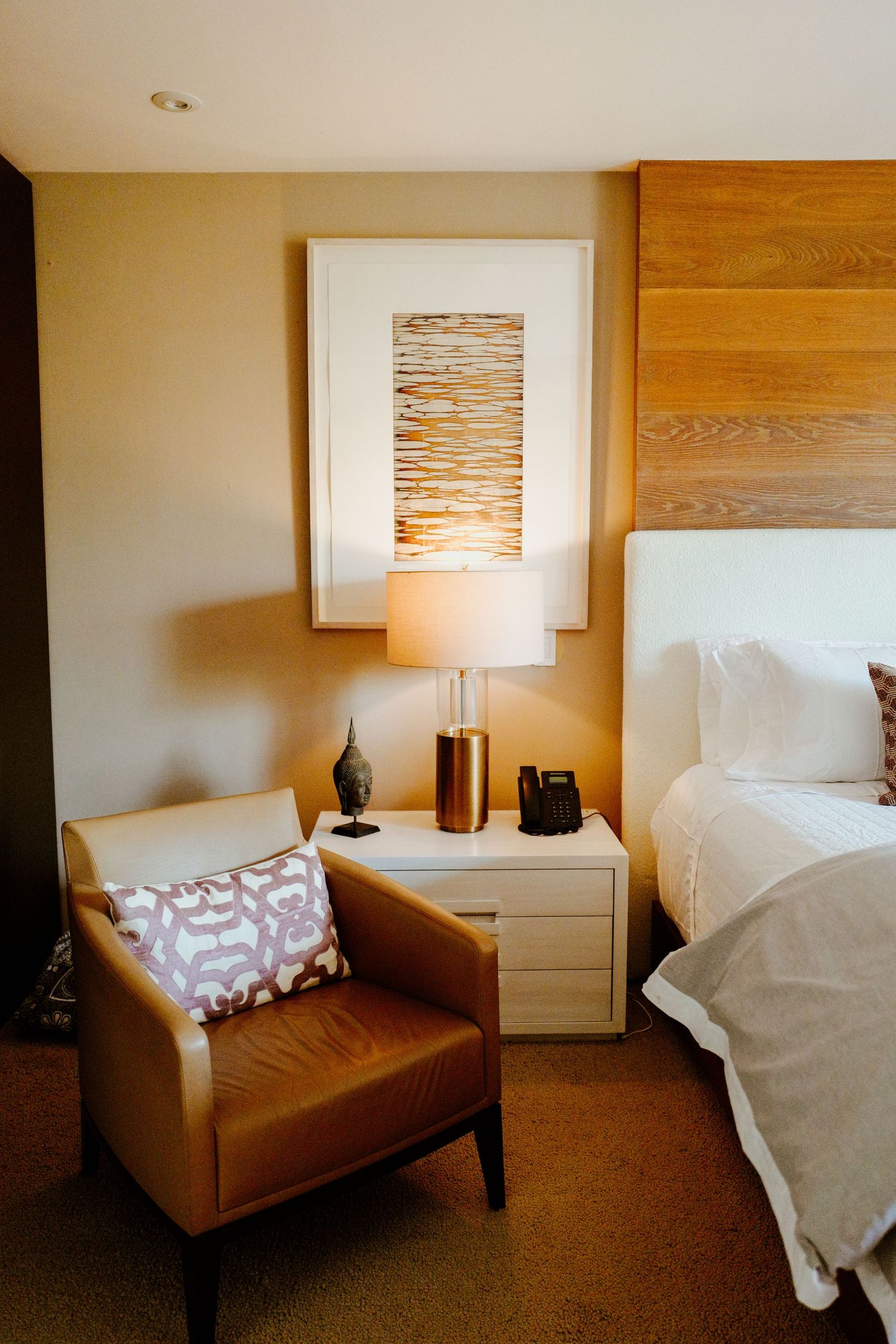 Cozy hotel bedroom corner with leather chair, nightstand lamp, and framed wall art.