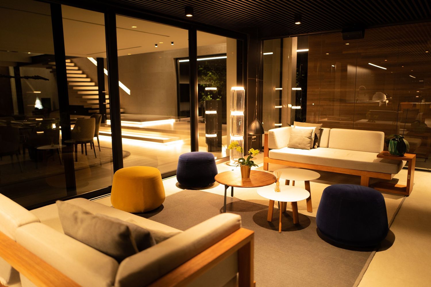 Warm modern lounge with colorful accent chairs, wooden tables, staircase, and soft ambient lighting.