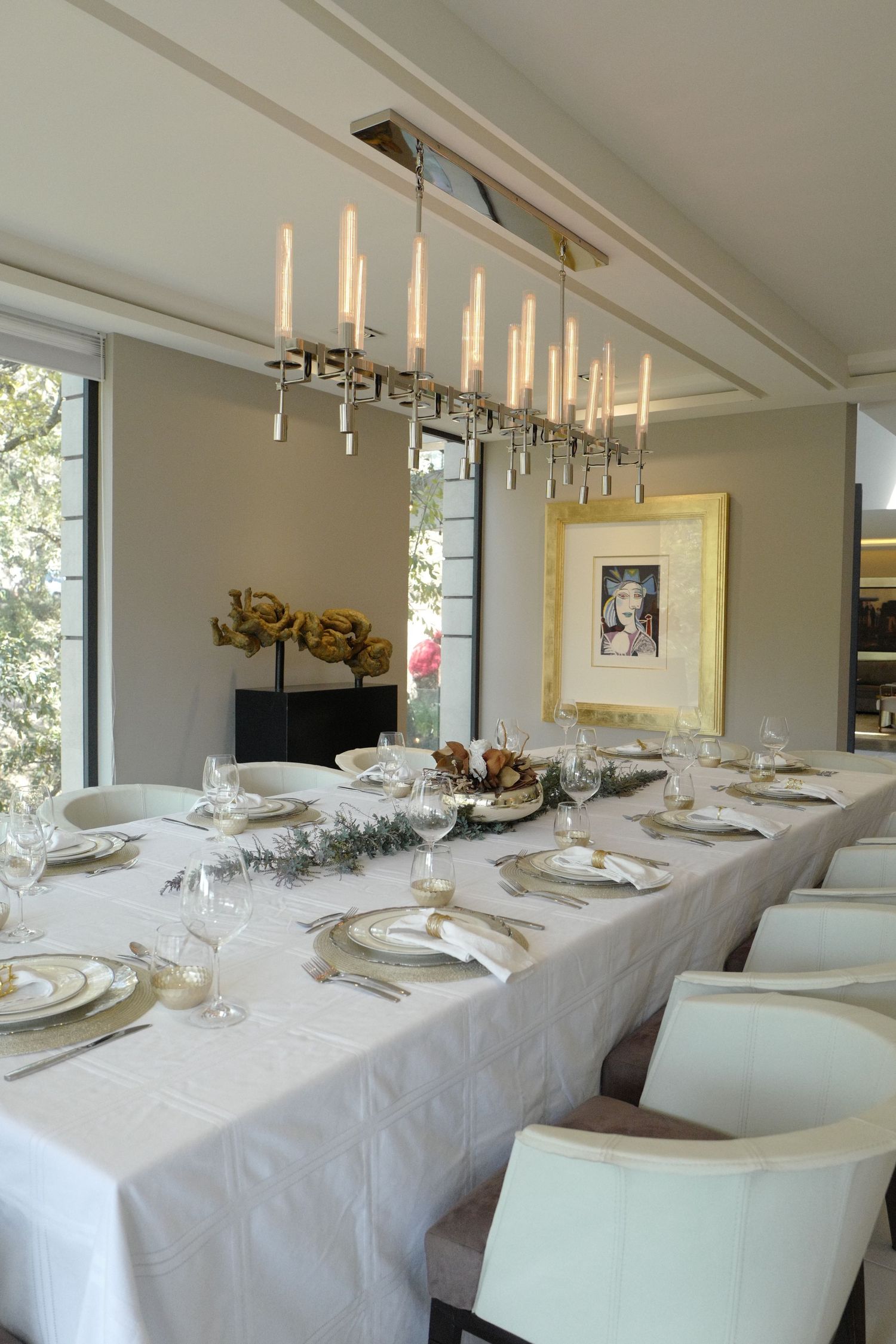 Elegant formal dining room with long white tablecloth, candle chandelier, and gold-framed artwork.