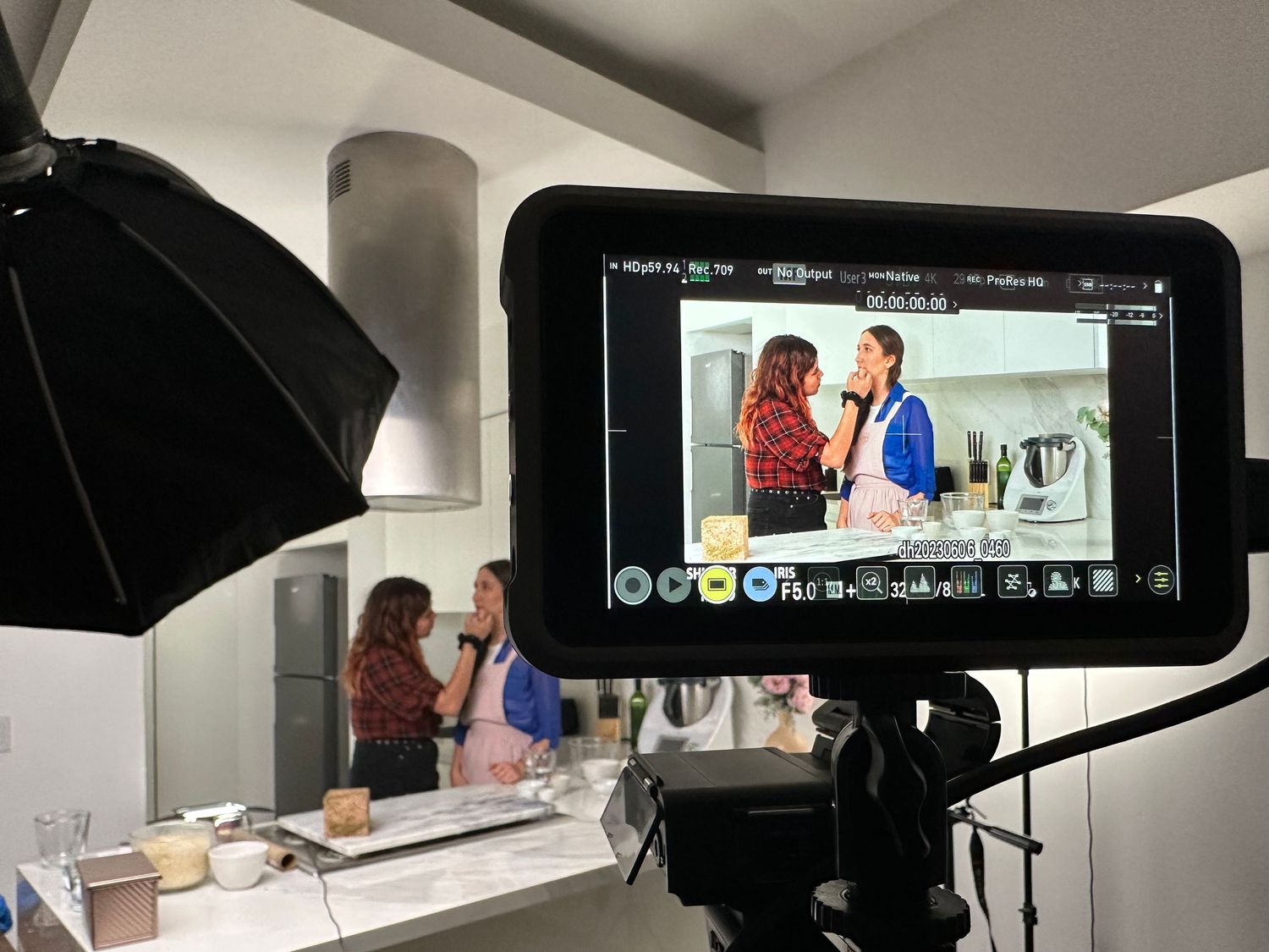 Camera monitor shows two women cooking in kitchen during culinary video production shoot.