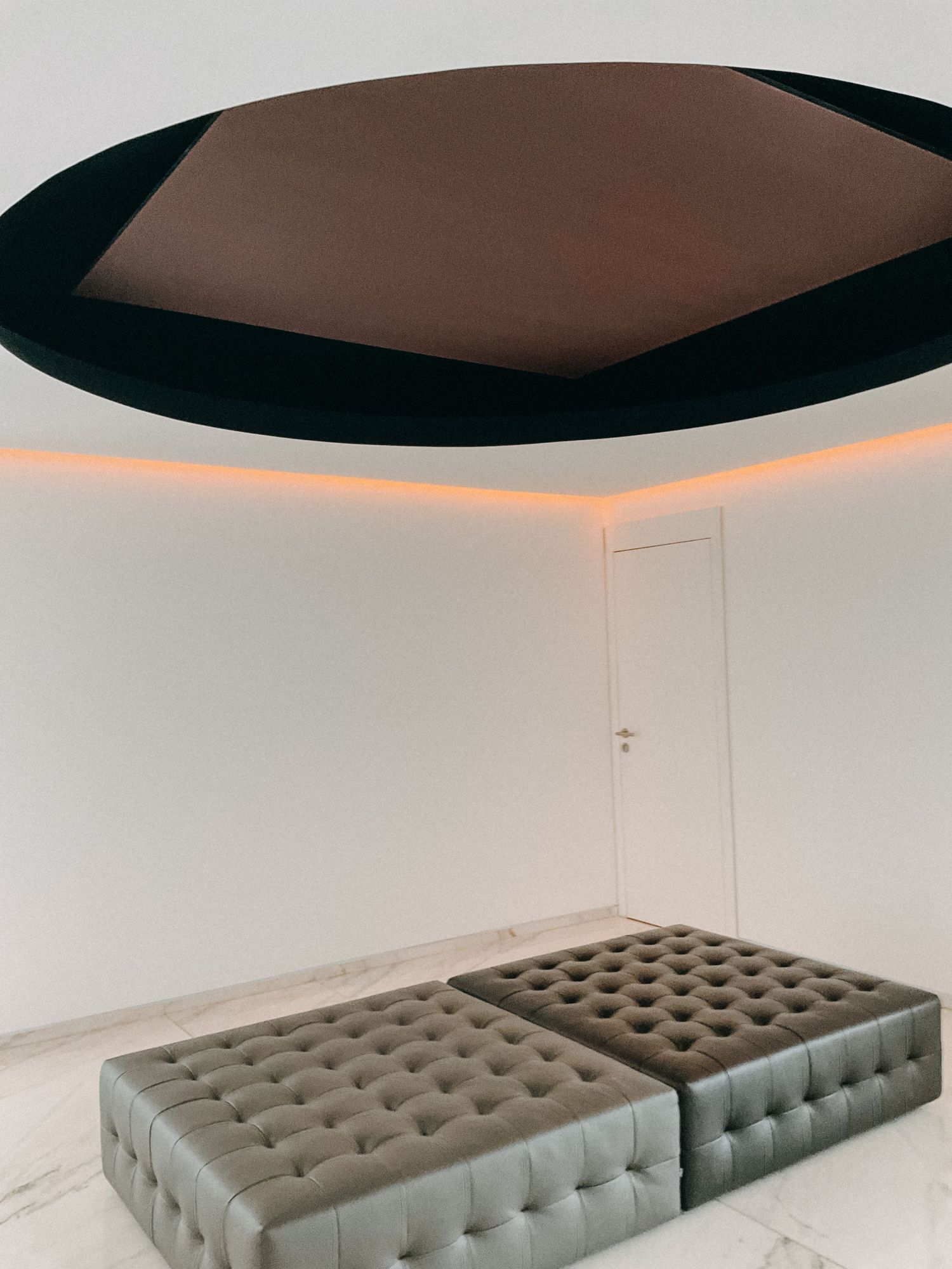 Luxury room with tufted silver ottomans beneath a dramatic oval skylight with ambient lighting.