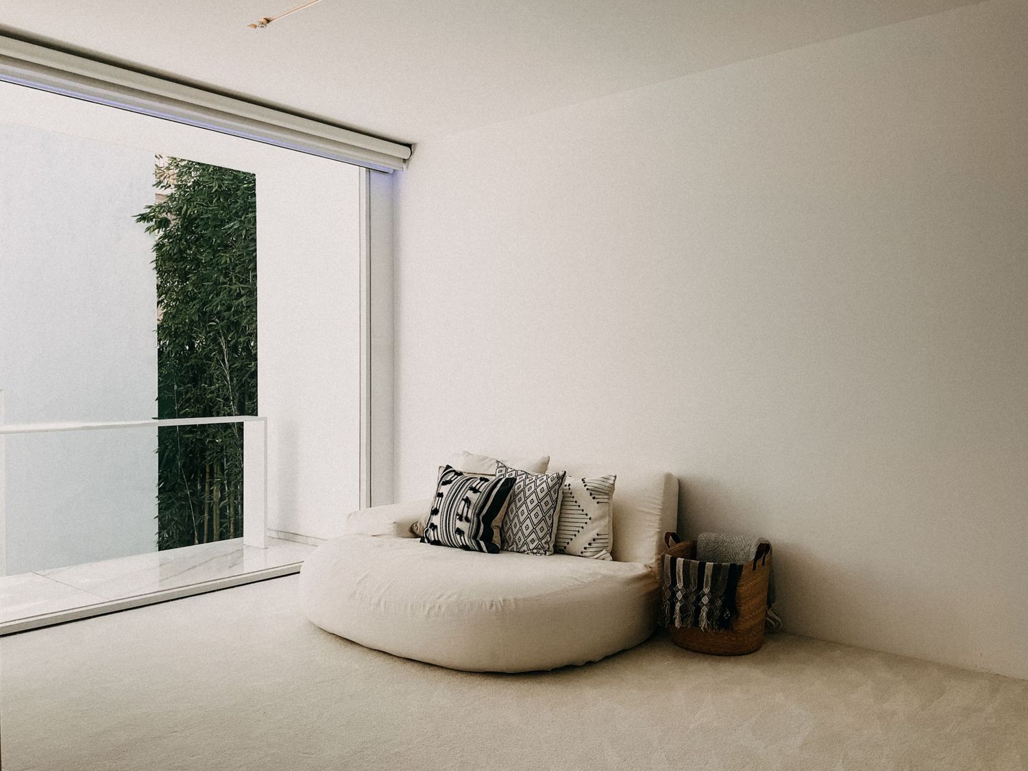 Minimalist living room with a round cream sofa, decorative pillows, and a large window overlooking a balcony.
