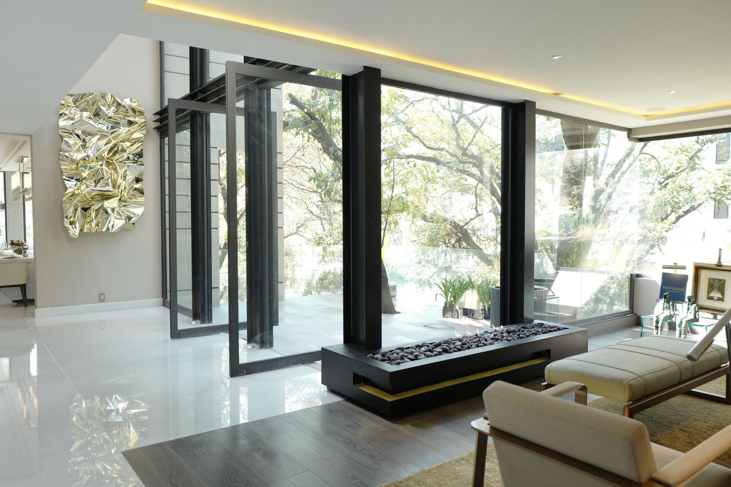 Minimalist modern living room with floor-to-ceiling glass windows, gold wall art, and marble floors.