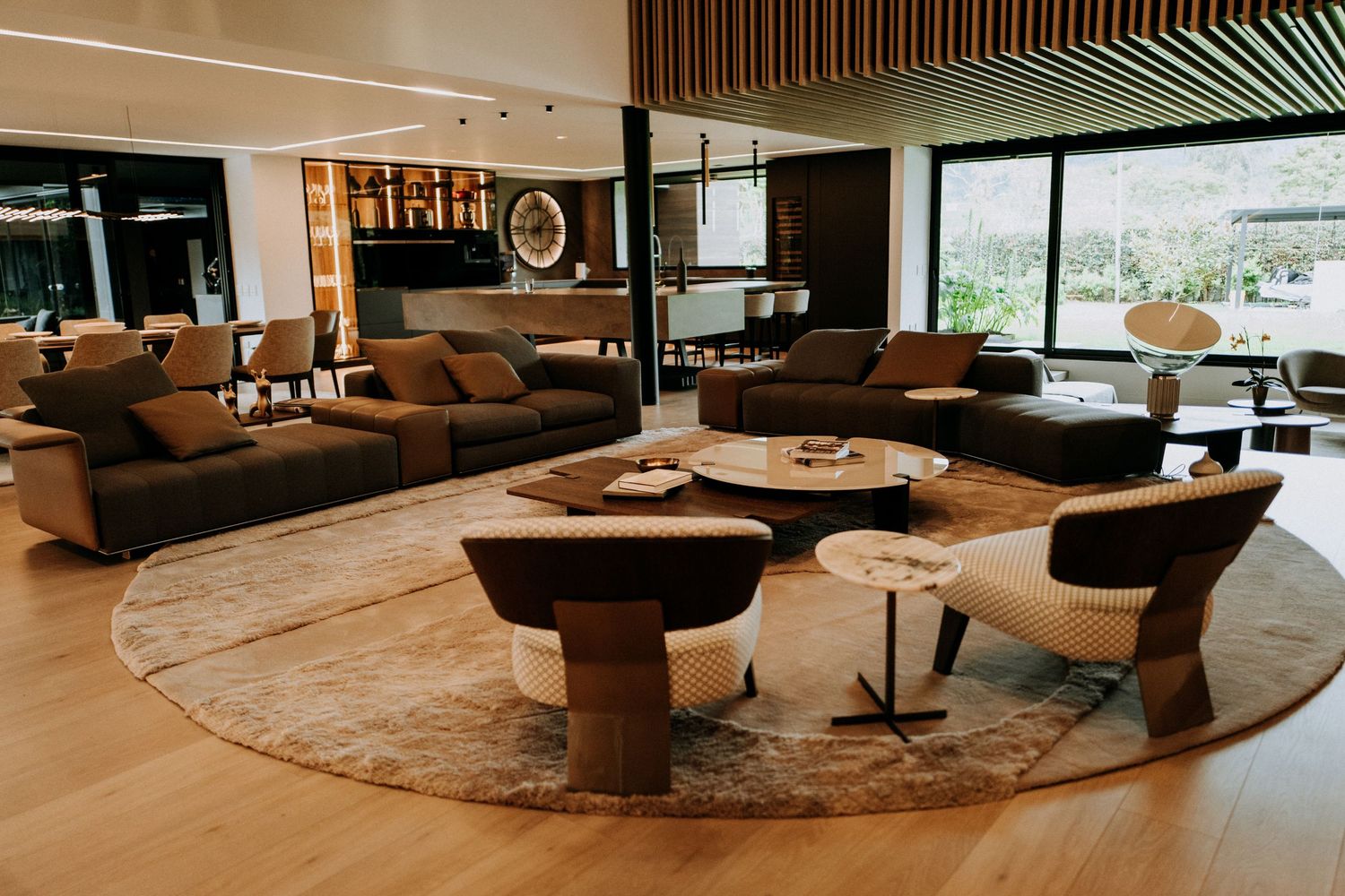 Spacious luxury living room with brown sofas, round rug, wooden ceiling, and open floor plan.