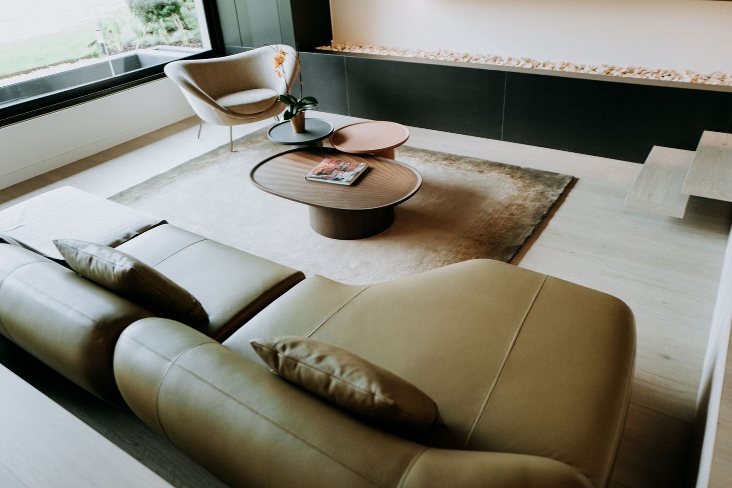 Aerial view of minimalist living room with beige leather sofas, round wooden coffee table, and fireplace.