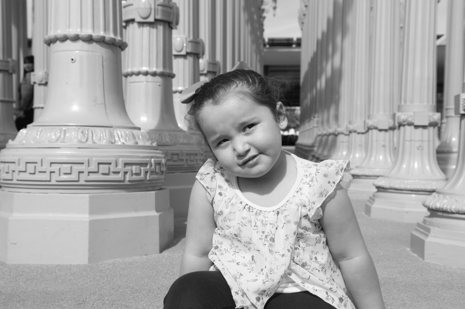 Black and white portrait of a toddler girl sitting near decorative columns.