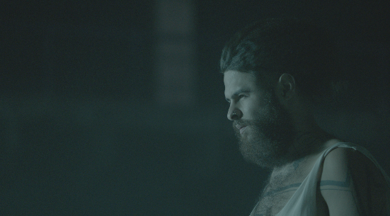 A bearded man is dramatically lit in a moody teal-toned cinematic portrait shot.