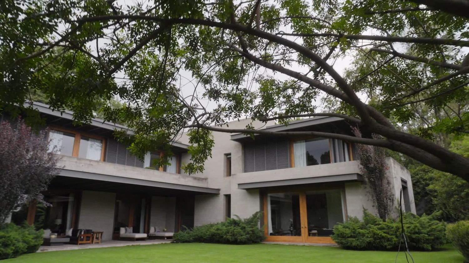 Elegant two-story house exterior with lush green lawn and mature trees in overcast daylight.