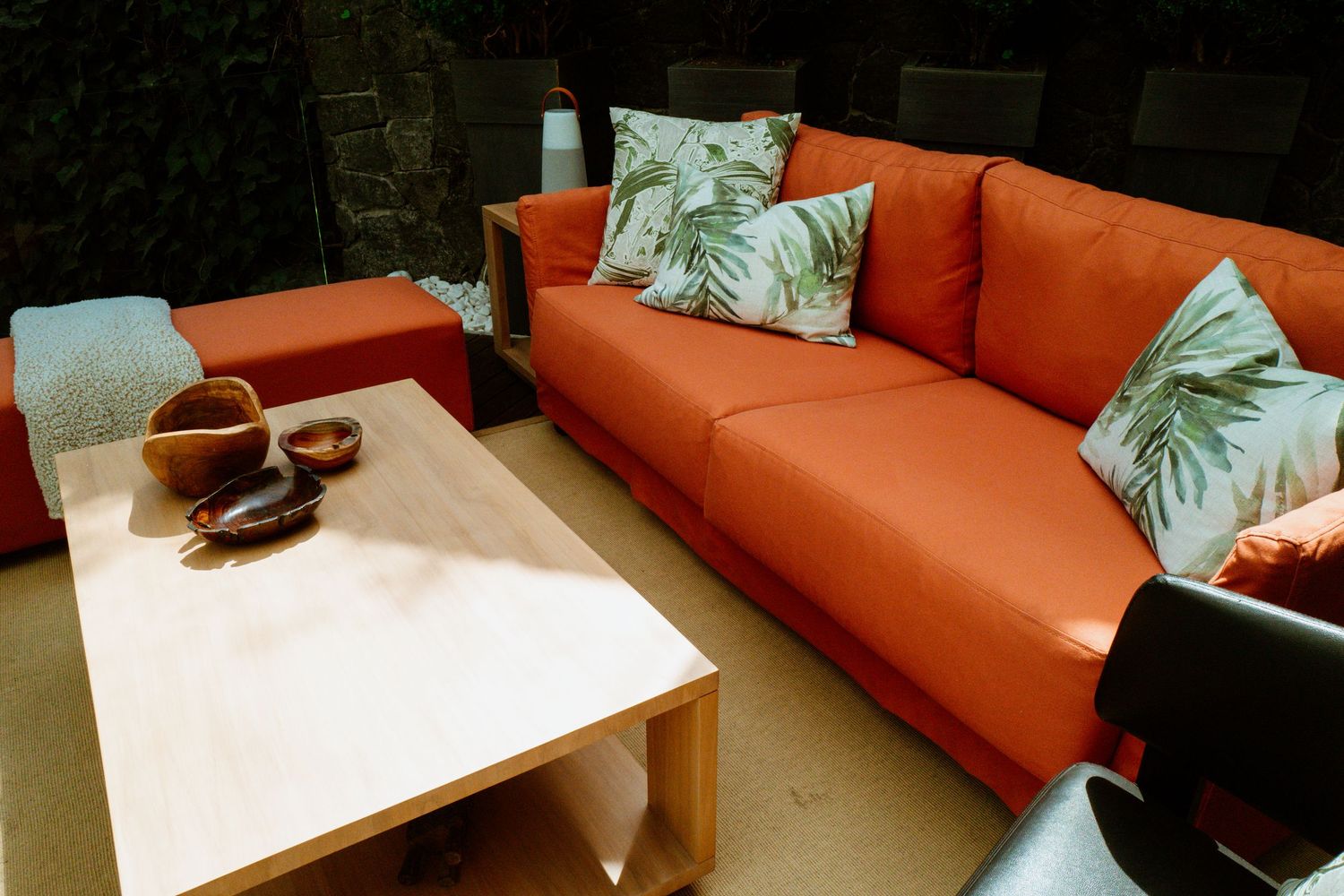 Orange outdoor sofa with tropical print pillows beside a wooden coffee table on a patio.