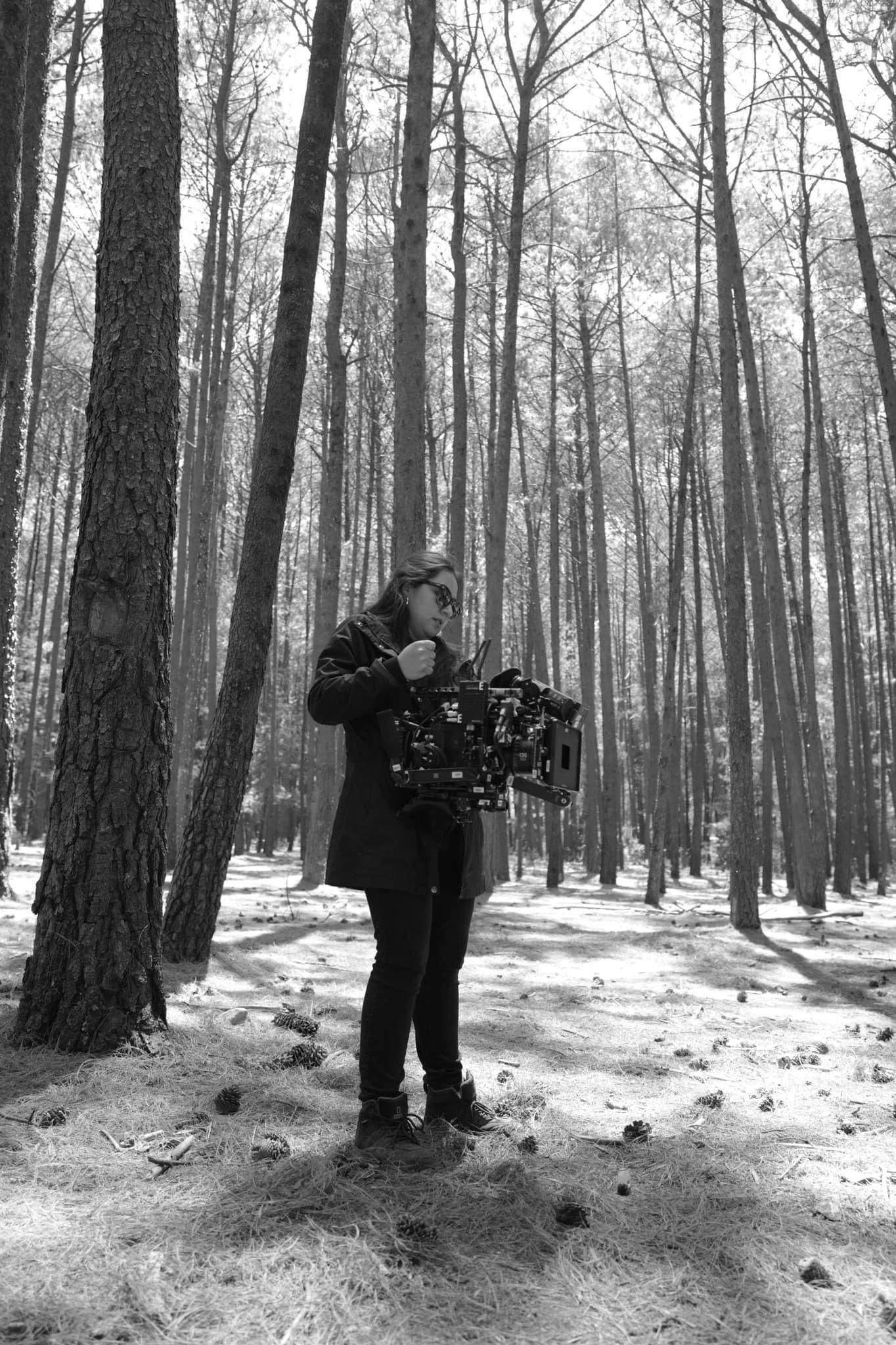 Black and white photo of cinematographer holding camera rig in pine forest location.