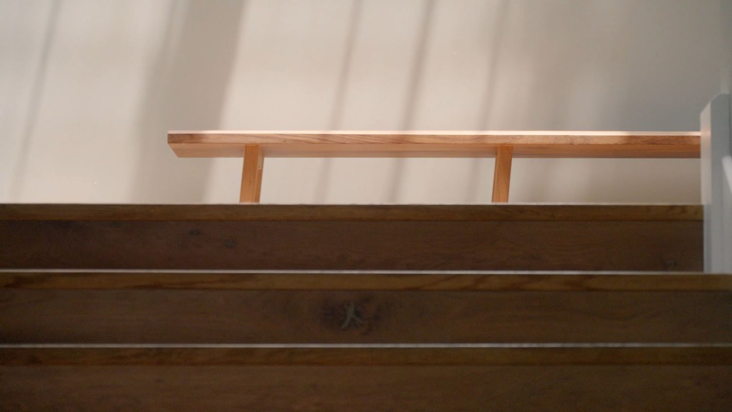 Close-up of wooden staircase with copper handrail casting geometric shadows on white wall.