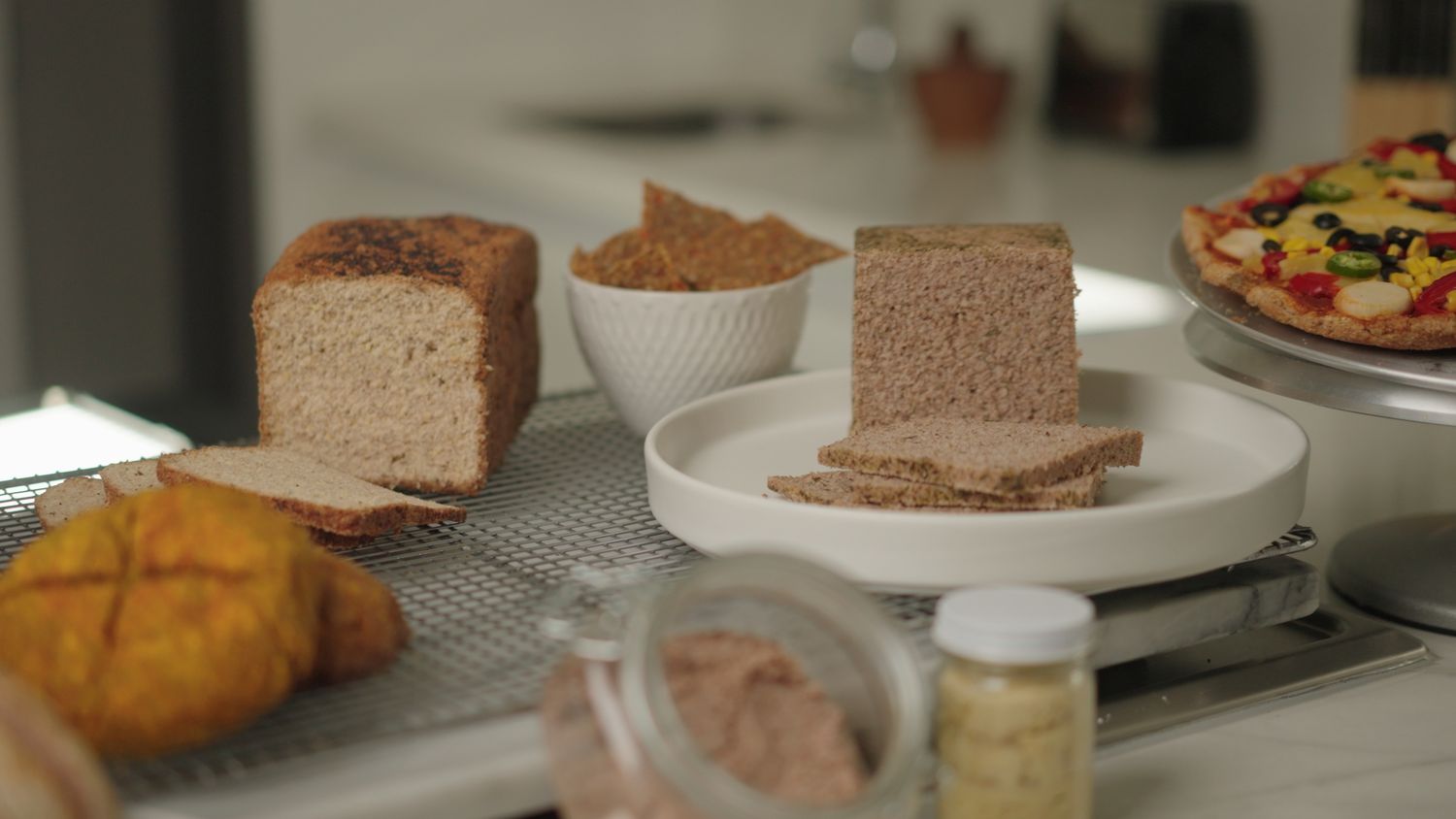 Assorted artisan breads and pizza displayed on a kitchen counter in natural light.