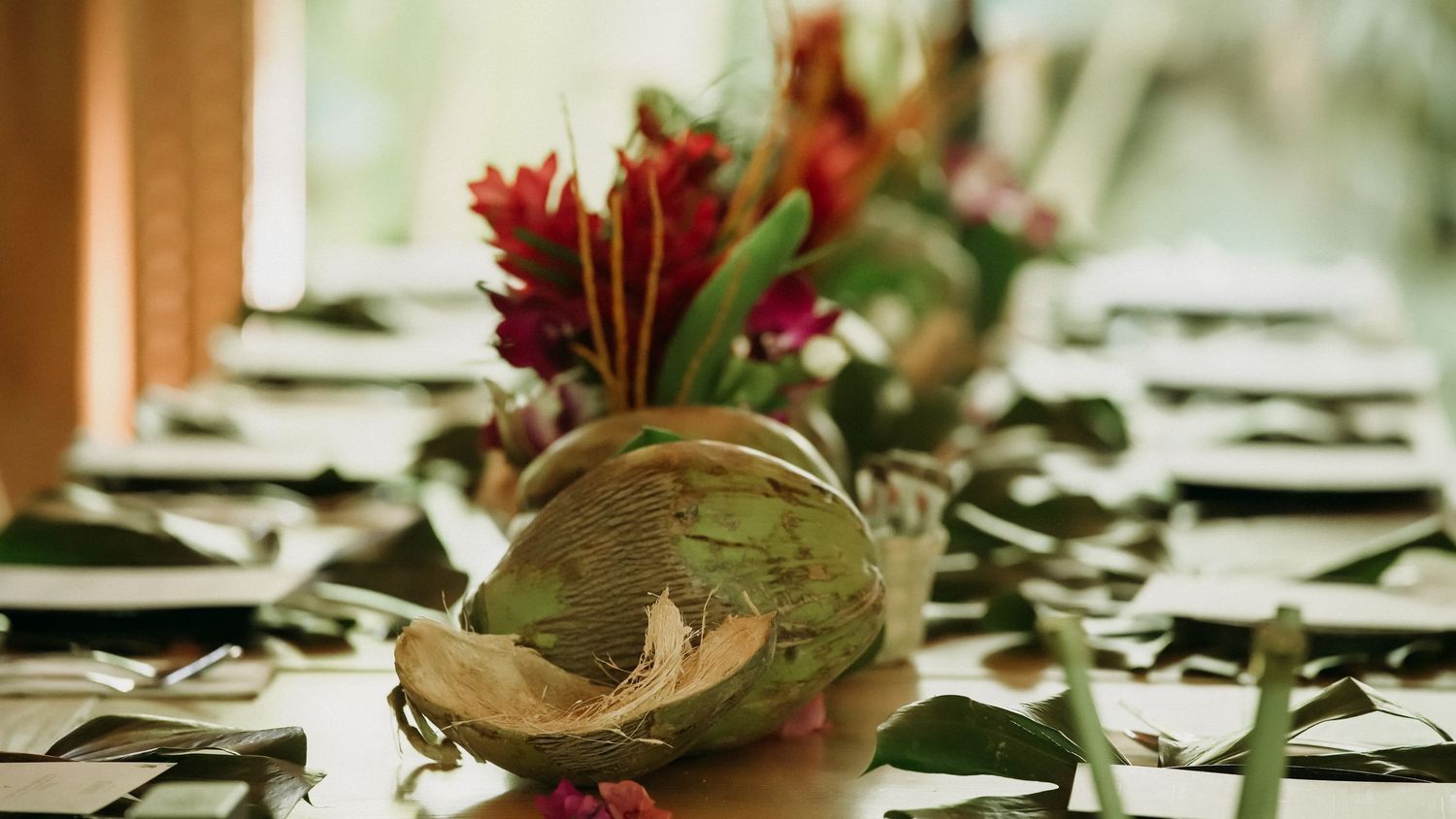 Close-up of tropical table centerpiece featuring coconut and red ginger flowers on green leaves.