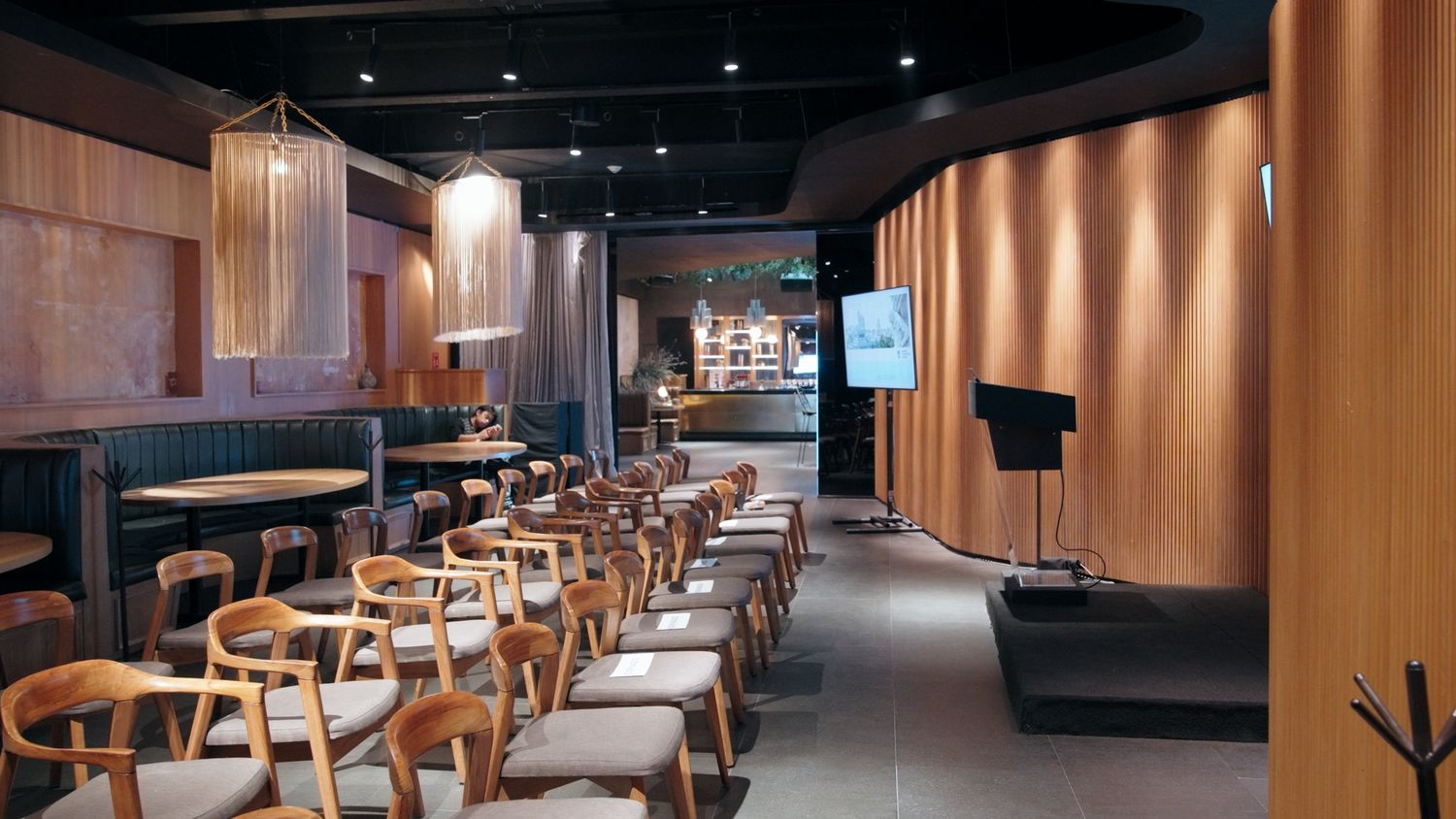 Modern restaurant interior with wooden chairs, pendant lights, and warm wood-paneled walls.