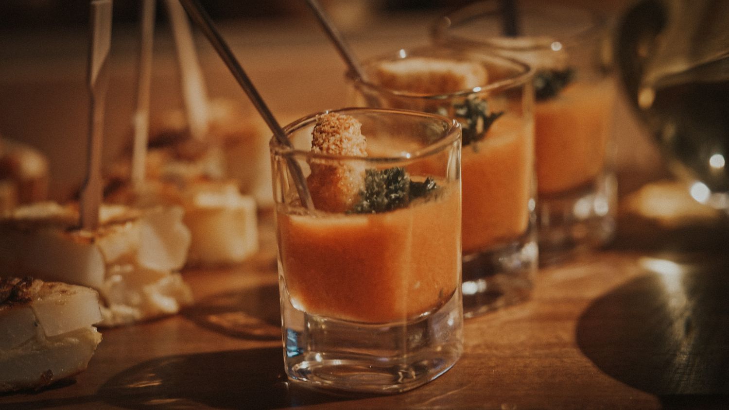 Elegant gazpacho soup shots garnished with herbs served in glass cups at a party.