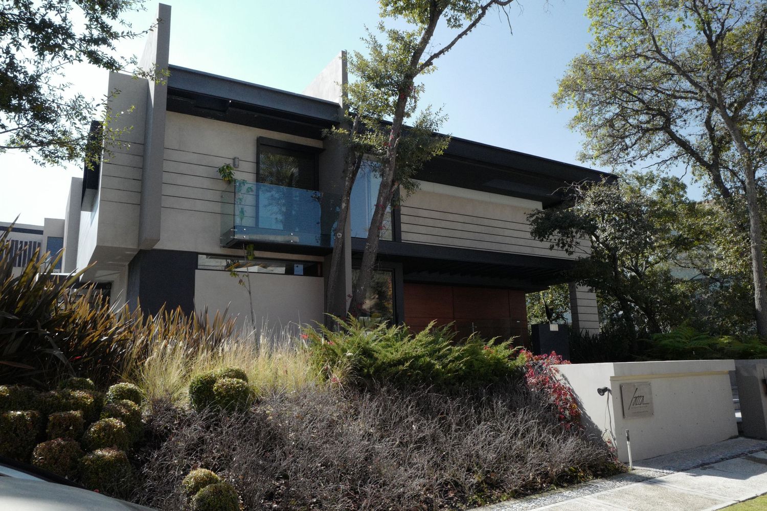 Modern two-story contemporary home with geometric architecture, balcony, and landscaped garden.