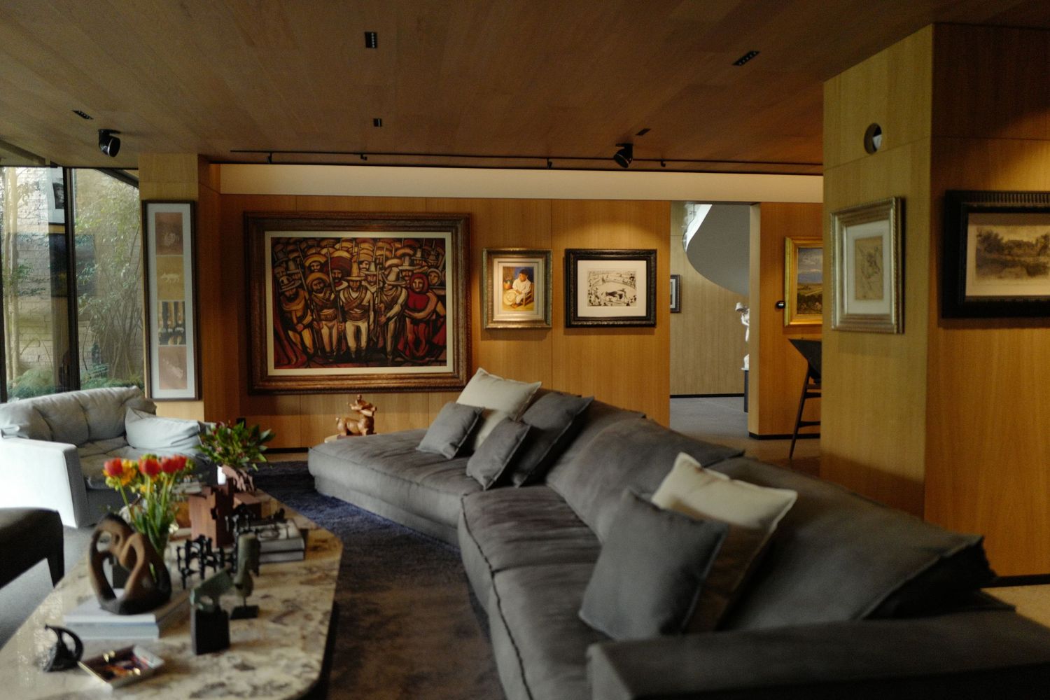 Cozy wood-paneled living room with large gray sectional sofa, artwork collection, and garden window.