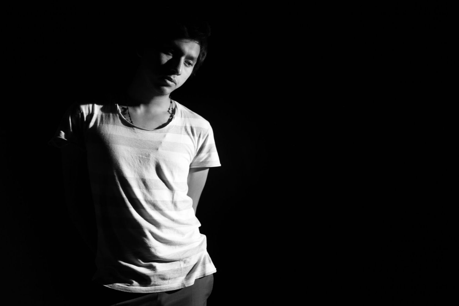 A young man in a white t-shirt poses dramatically in a high contrast black and white portrait.