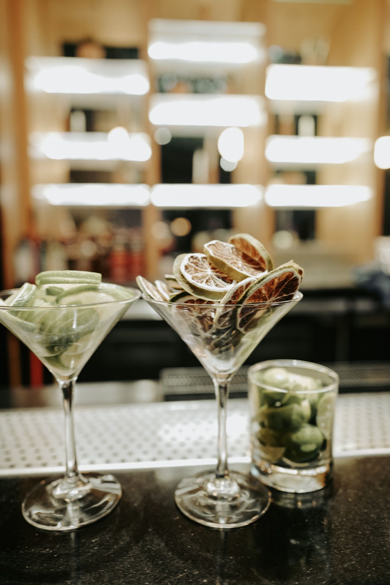 Two martini glasses filled with dried citrus slices and cucumber garnishes on a bar counter.