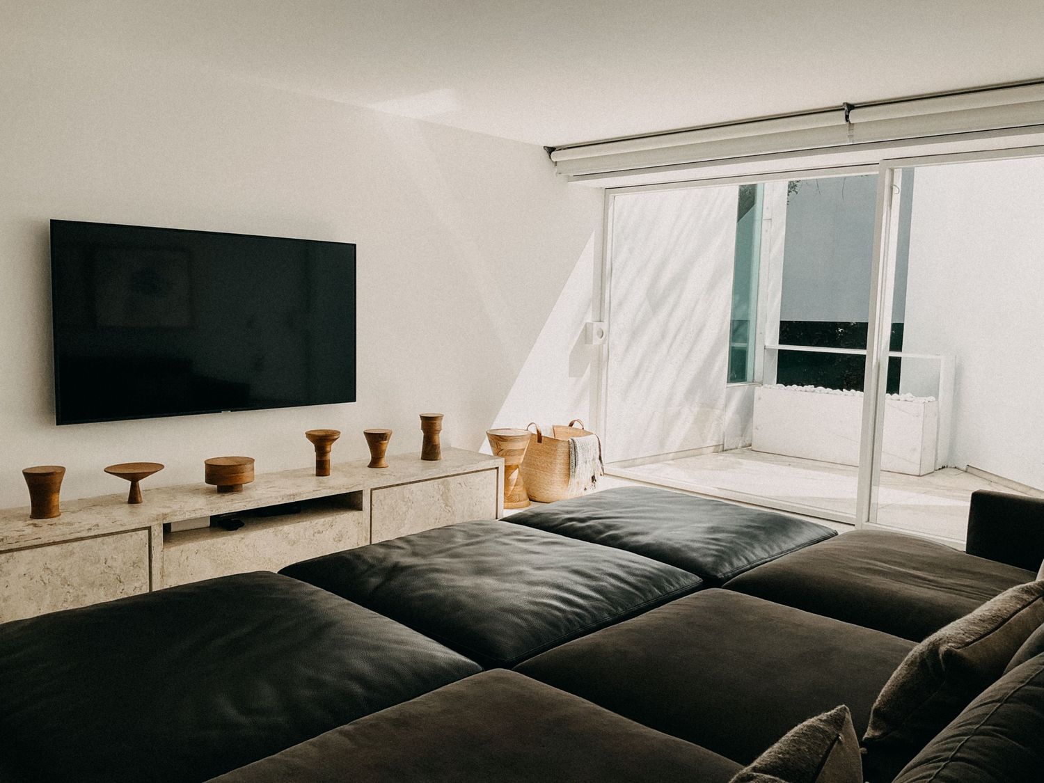 Modern minimalist living room featuring oversized dark sofa, mounted TV, and bright glass sliding door.