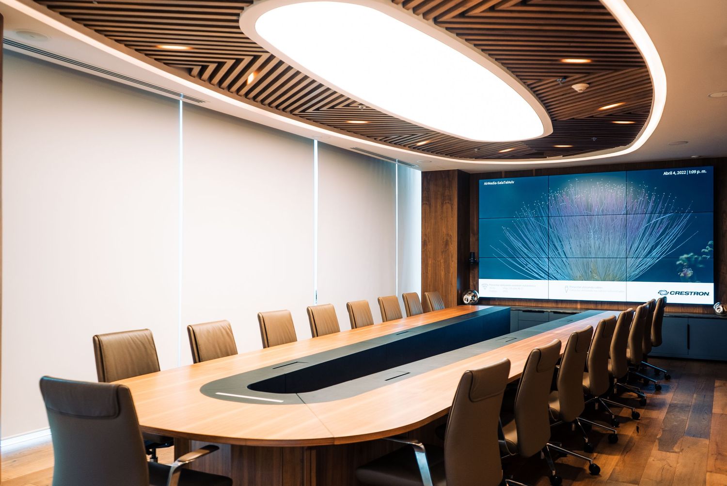 Elegant corporate boardroom with oval table, leather chairs, wood ceiling, and large display screen.