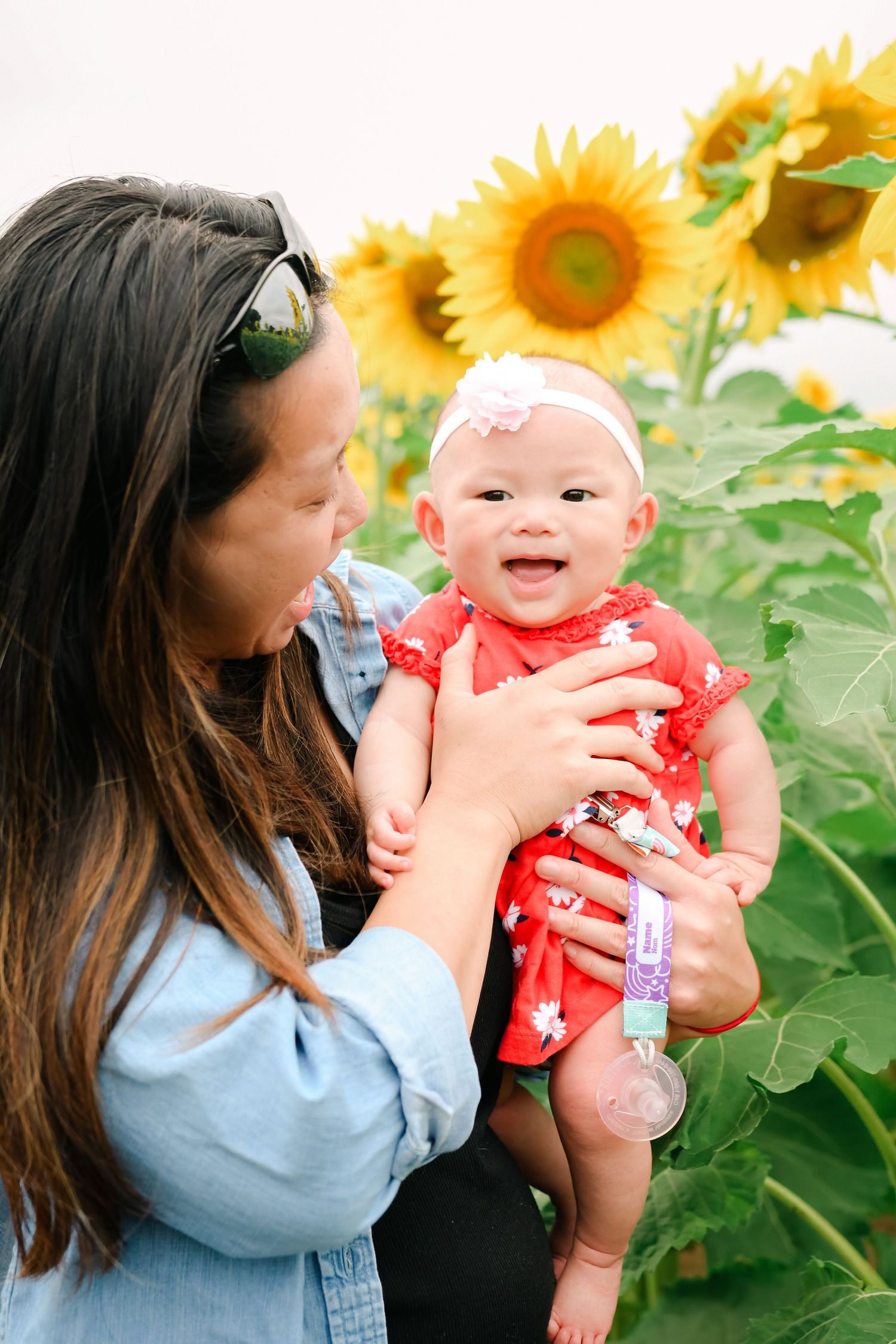 Luminous lifestyle portrait of a mother holding her baby in a sunflower field.
