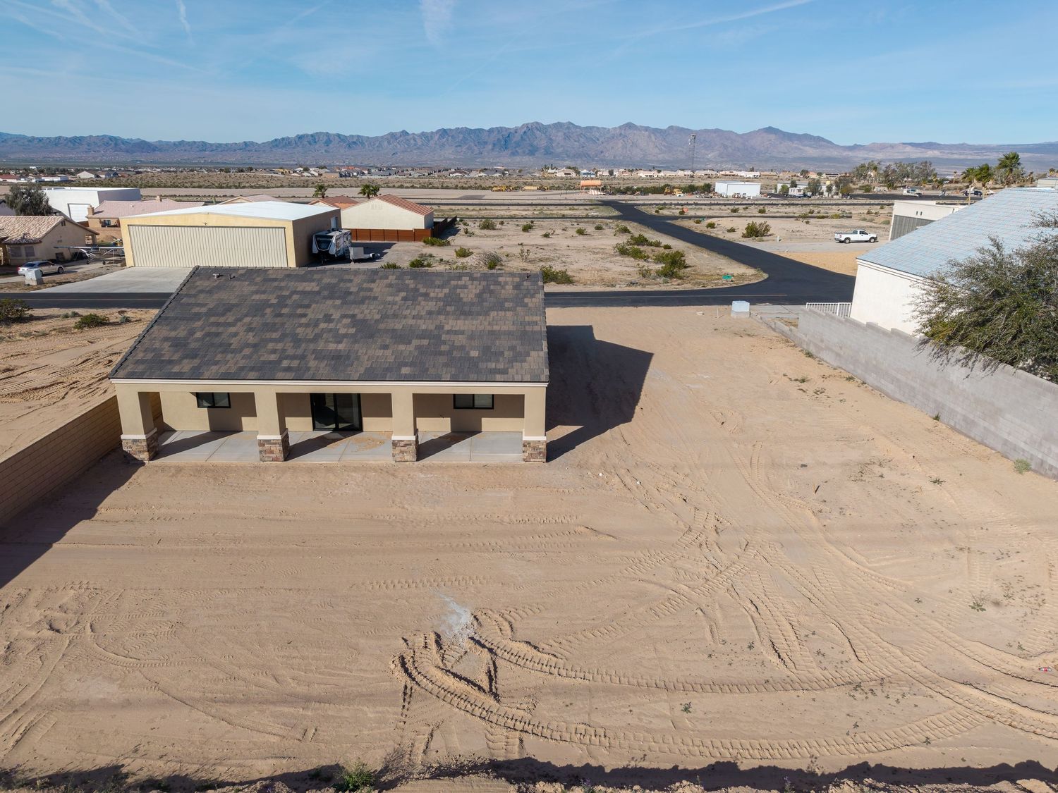 Aerial view of a desert construction site with dirt plots and buildings in the background against mountain ranges.