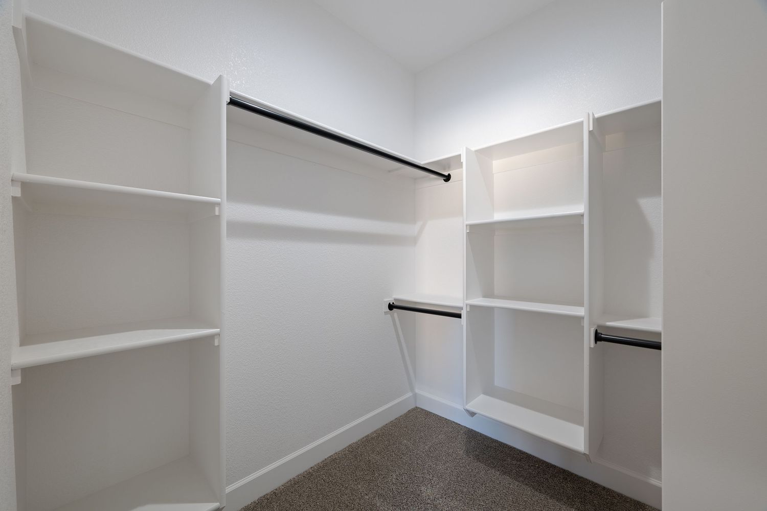 White built-in shelving and storage cabinets line the walls of a bright walk-in closet with hanging rods.