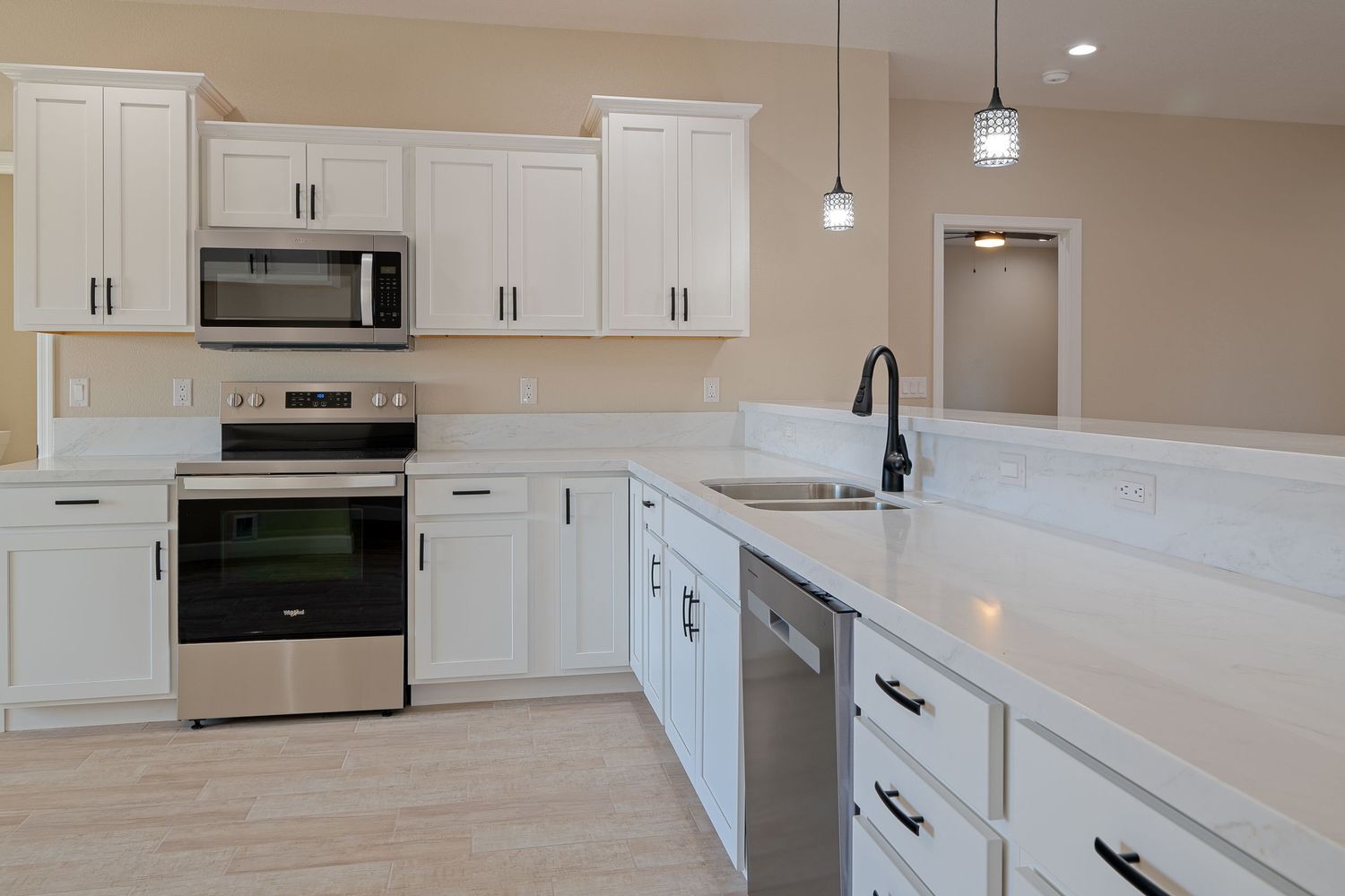 Modern white kitchen with quartz countertops, pendant lights, and stainless steel appliances showcases clean lines and bright design.