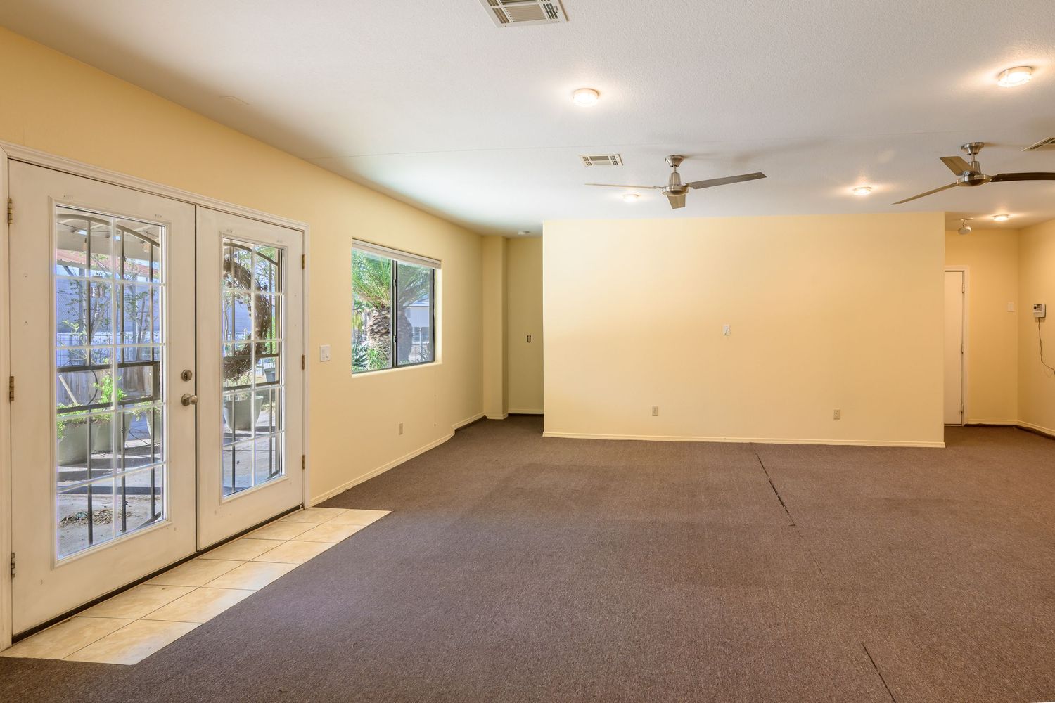 Large empty commercial space with white walls, ceiling fans, and windows showing natural light along one side.