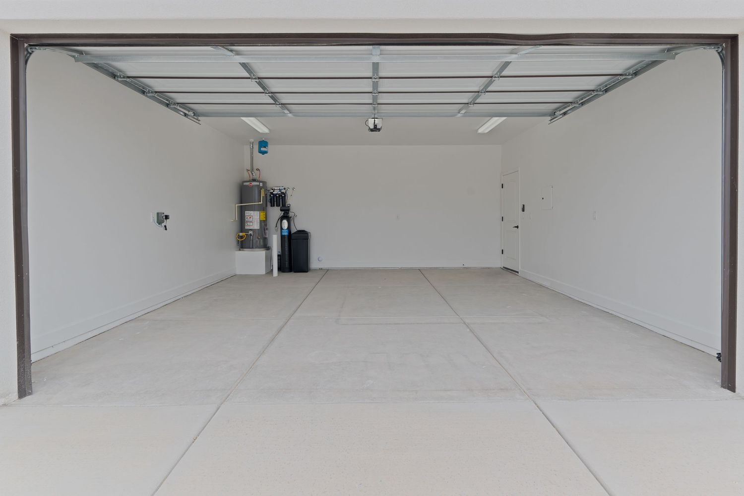 Spacious empty two-car garage with white walls, clean epoxy floor, and automatic garage door opener installed.