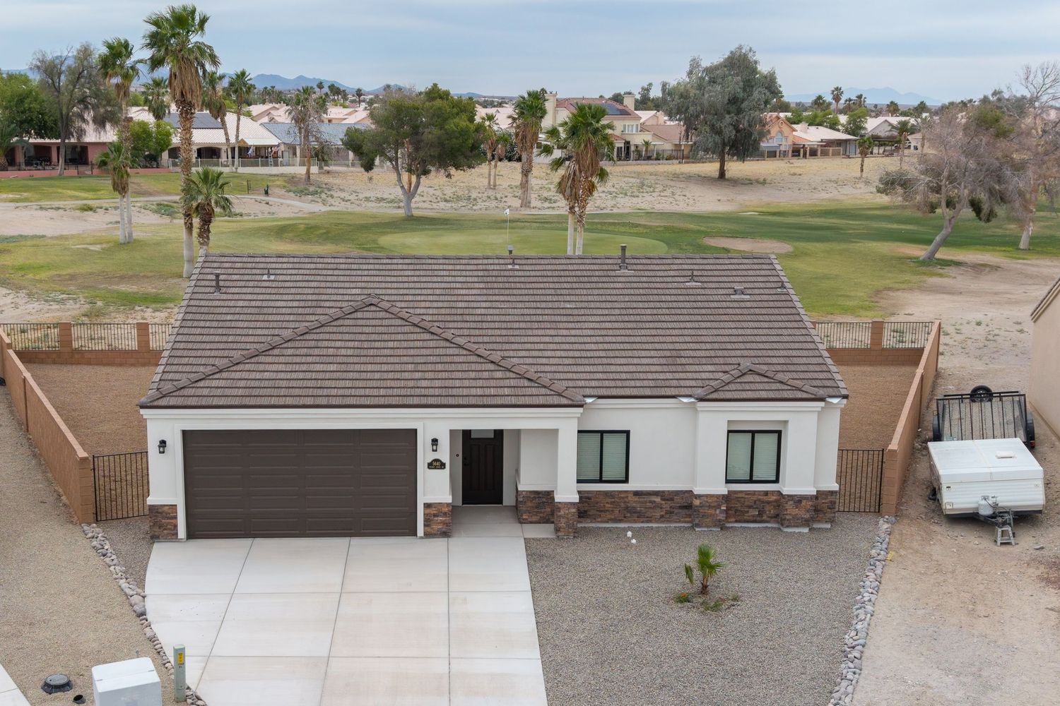 Aerial view of a single-story white stucco home with brown garage door, tile roof, and desert landscaping in a sunny Southwest neighborhood.