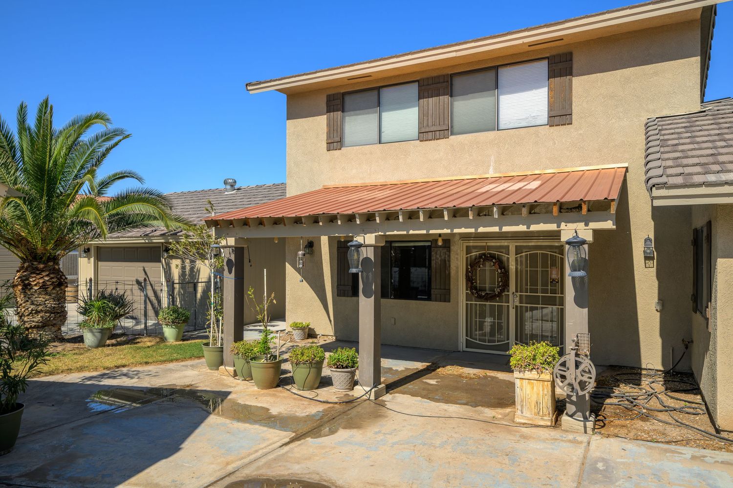 Exterior view of a modern beige stucco house with palm trees and desert landscaping in a residential neighborhood.