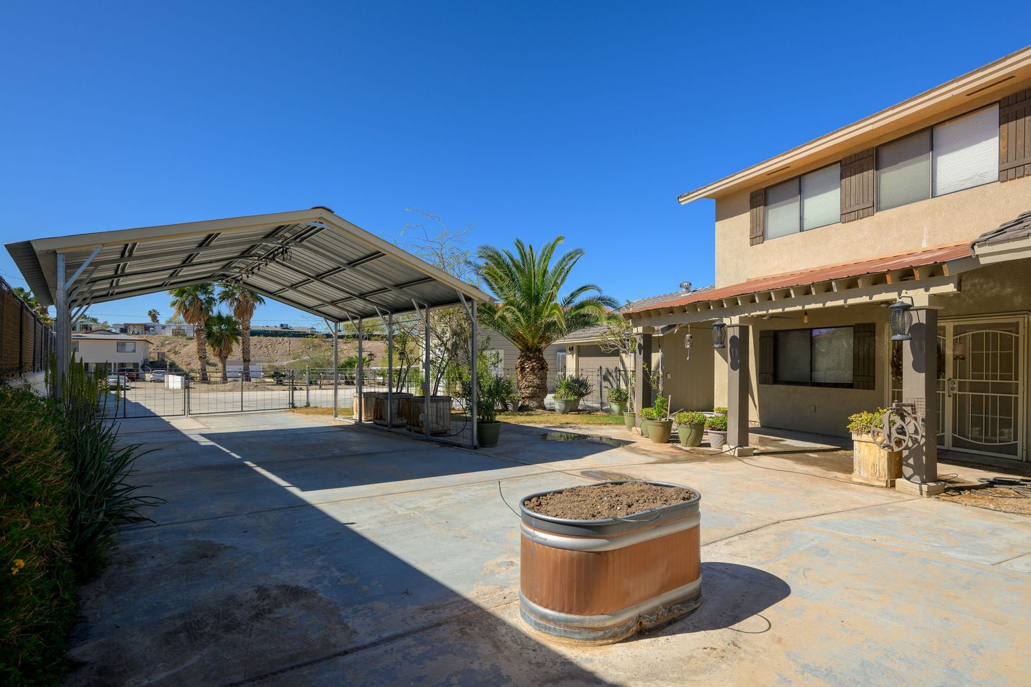 Panoramic view of a desert backyard with brown raised planter boxes and palm trees against a clear blue sky.