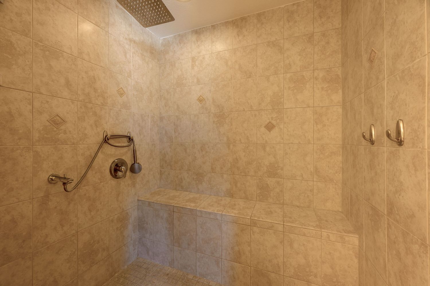 Beige tiled bathroom ceiling with recessed lighting and exposed ventilation ductwork.
