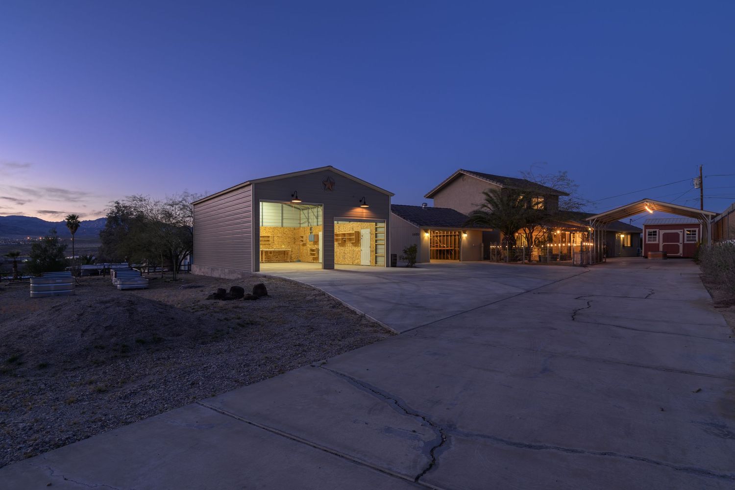 A panoramic desert landscape at dusk with illuminated buildings and winding roads against a deep blue sky.