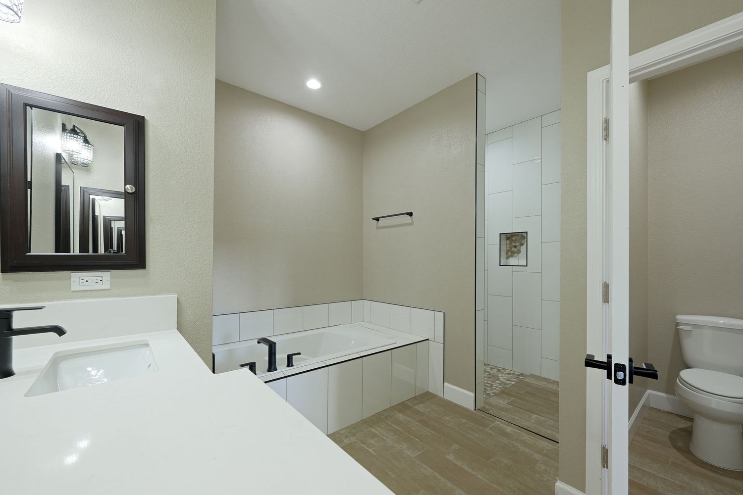 A modern white bathroom with recessed lighting features a glass shower enclosure and sleek fixtures.