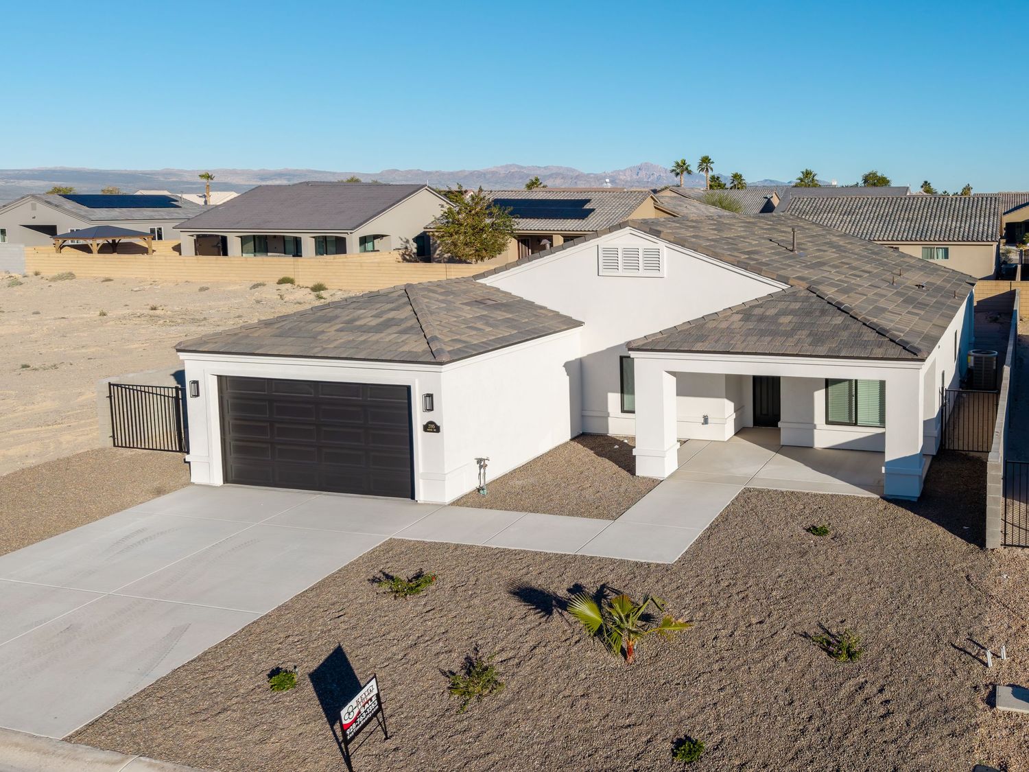 Aerial view of a modern white single-story house with gray roof and two-car garage in a desert neighborhood setting.