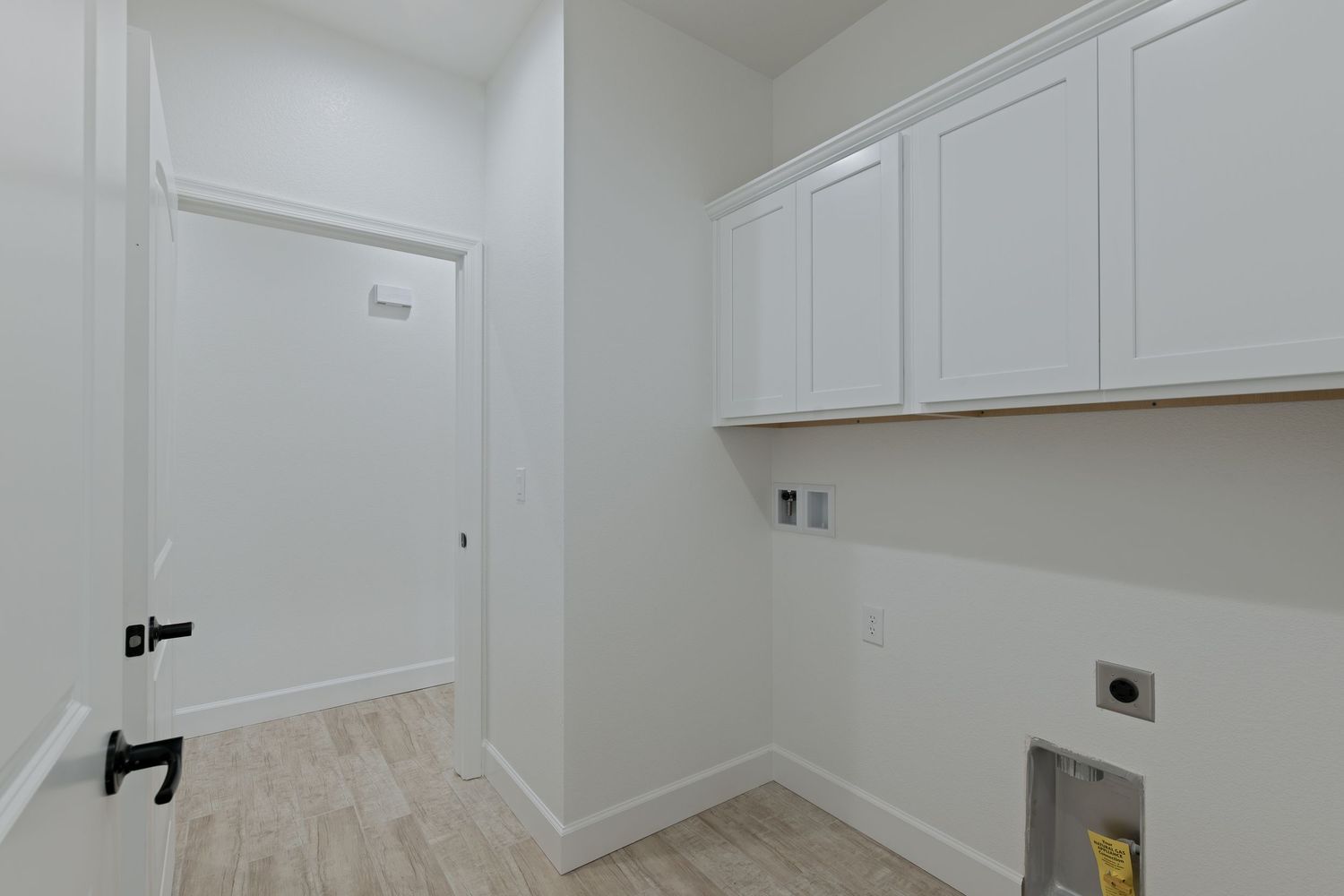 Bright laundry room with white shaker cabinets, washer and dryer hookups, and light wood-look flooring.