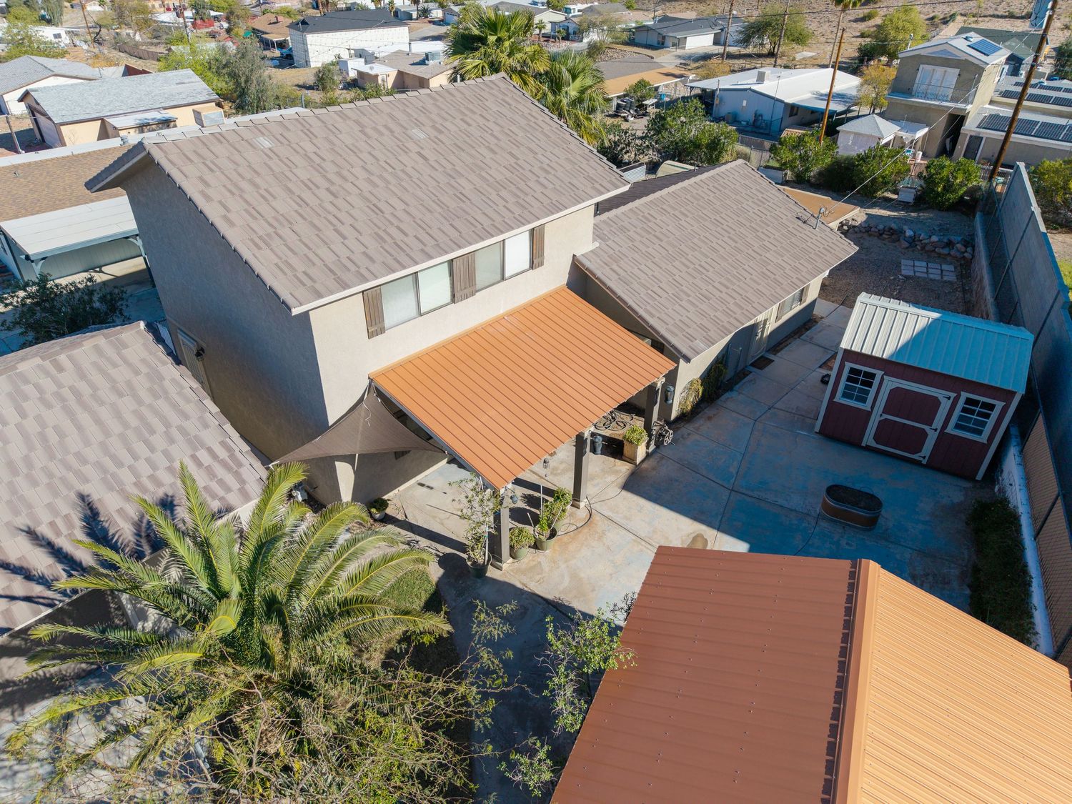 Aerial view of residential neighborhood with tiled roofs and palm trees on a sunny day.
