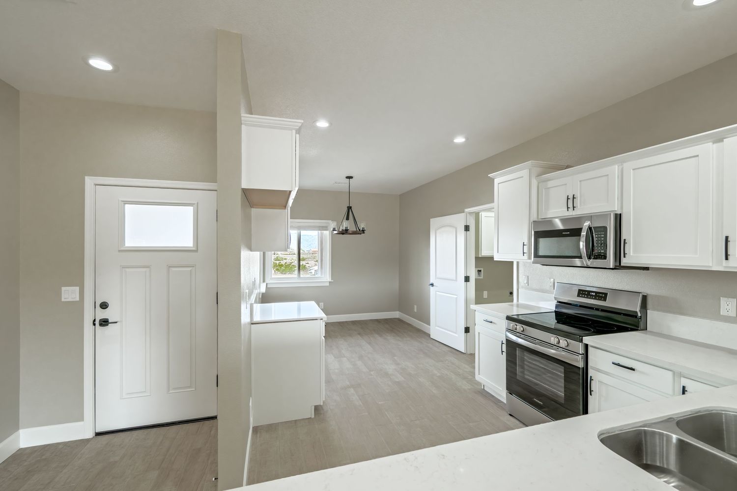 Modern white kitchen with stainless steel appliances, quartz countertops, and recessed lighting in an open concept layout.