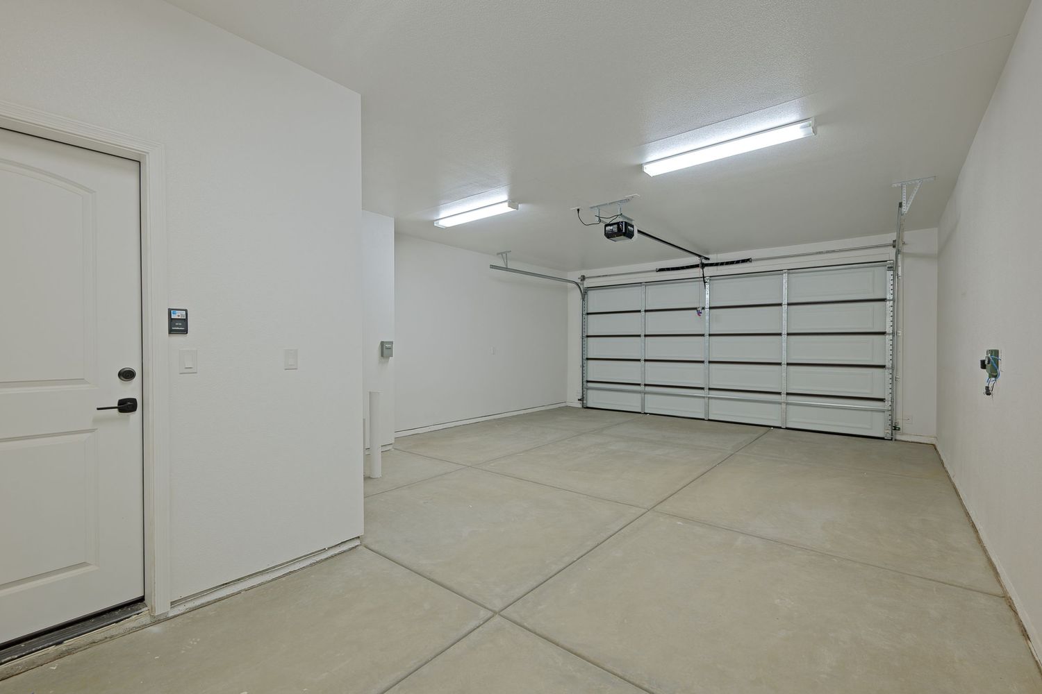 Clean interior of an empty residential garage with white walls, fluorescent lighting, and a sectional garage door.
