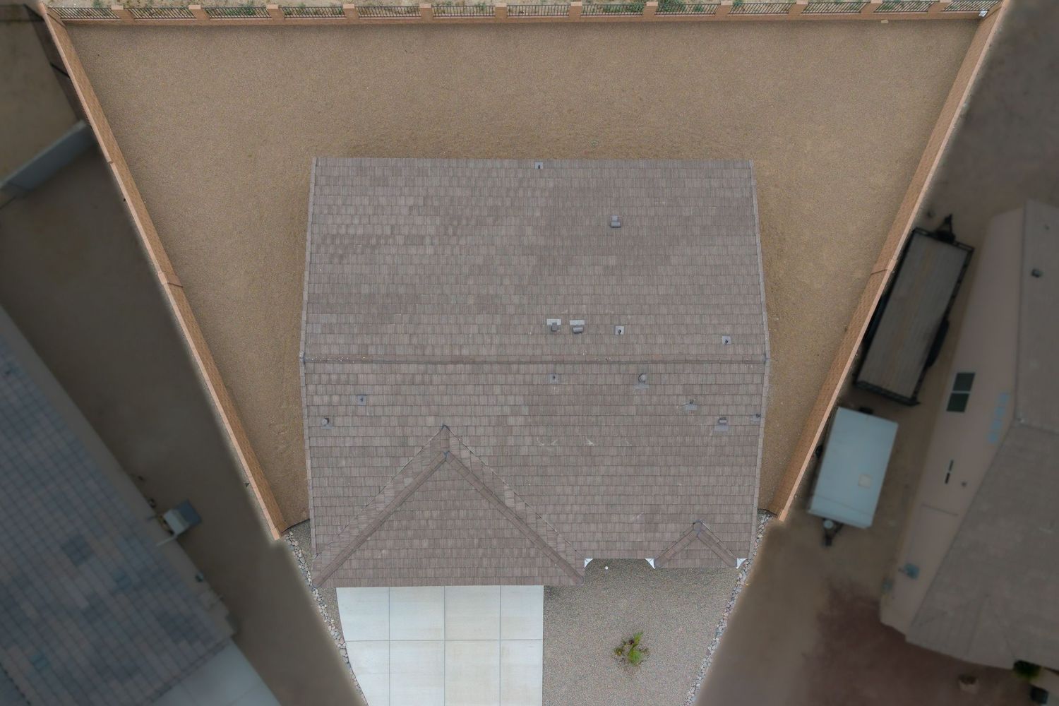 Aerial view of a residential home with gray shingle roof surrounded by tan stucco walls.