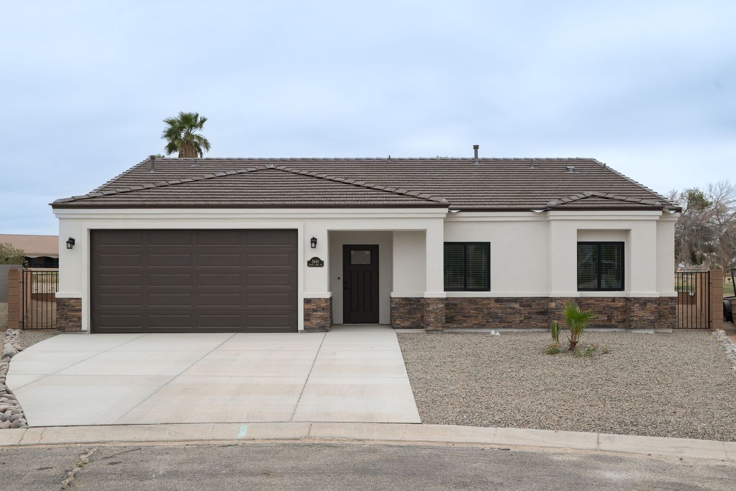 Modern single-story stucco home with dark brown garage door, stone accents, and desert landscaping in Arizona.