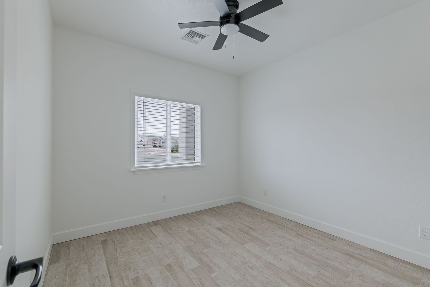 Empty bedroom with light wood floors, white walls, a ceiling fan, and a window with blinds.