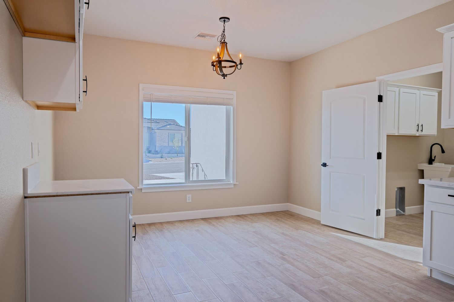 Empty room with light hardwood floors, beige walls, white trim and a pendant light fixture in a residential interior.