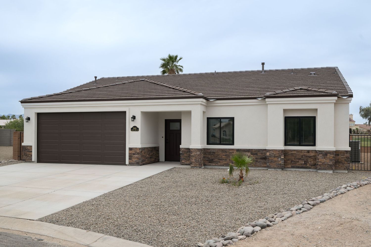 Single-story stucco home with brown garage door, stone accents, desert landscaping, and a wide driveway in Arizona.
