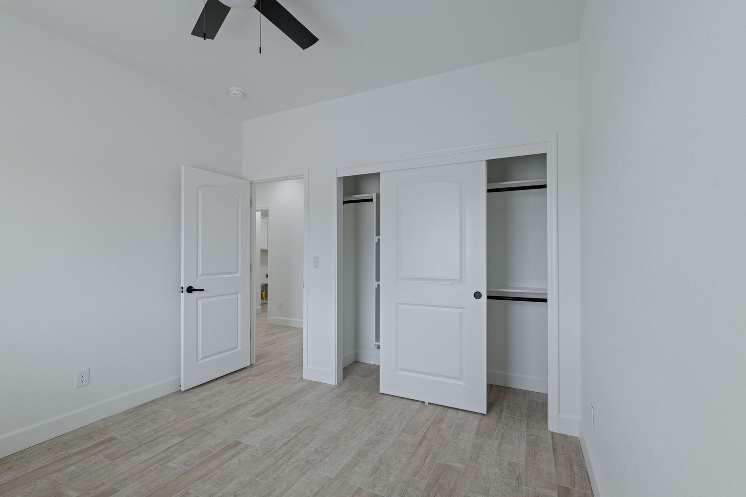 Empty bedroom with open closet, light wood floors, white walls, and ceiling fan in a modern home.