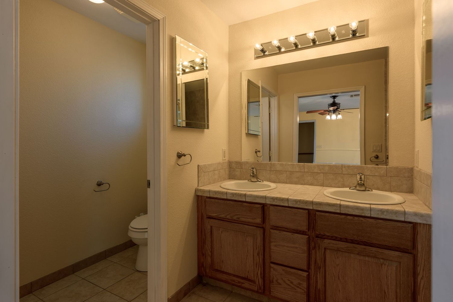 Bathroom interior with wooden vanity cabinet, granite countertop, framed mirror, and separate toilet room.